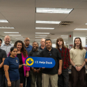 A group of ten diverse office workers posing together, one holding an I.T. Help Desk sign.